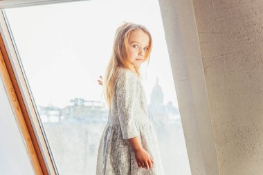 Evde kal. Kendine dikkat et. Beyaz elbiseli, sevimli, tatlı bir kız pencerenin pervazında duruyor. Evdeki parlak ışıklı oturma odasında. Çocukluk çocukları gençlik konsepti