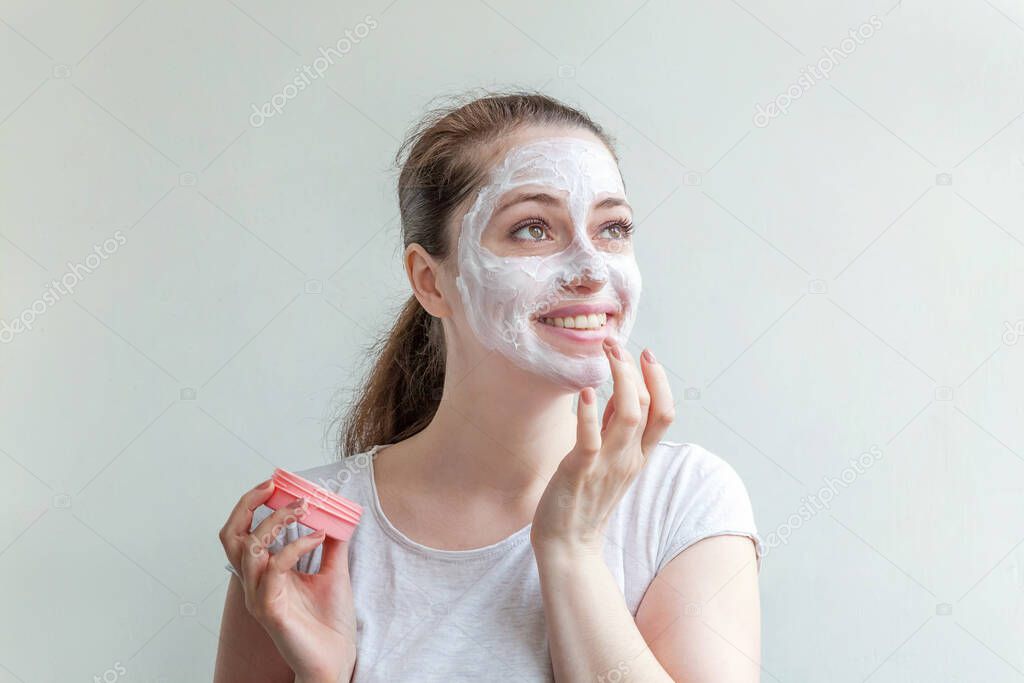 Minimal beauty portrait young woman girl portrait applying white nourishing mask or creme on face isolated on white background. Skincare cleansing eco organic cosmetic spa concept