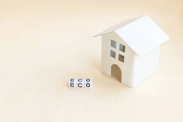 Miniature toy model house with inscription ECO letters word on wooden backdrop. Eco Village abstract environmental background. Ecology zero waste social responsibility recycle bio home concept