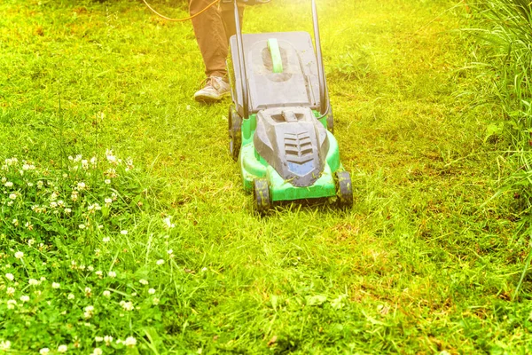 Man cutting green grass with lawn mower in backyard. Gardening country lifestyle background. Beautiful view on fresh green grass lawn in sunlight, garden landscape in spring or summer season
