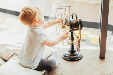 Evde kal. Kendine dikkat et. Evdeki parlak ışıklı oturma odasındaki geniş pencerenin yanında vantilatörlü vantilatörlü küçük tatlı bir kız bebek. Çocukluk ailesi annelik hassasiyeti kavramı