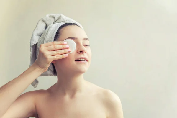 Beauty portrait of smiling woman in towel on head with soft healthy skin removing make up with cotton pad isolated on white background. Skincare cleansing spa relax concept