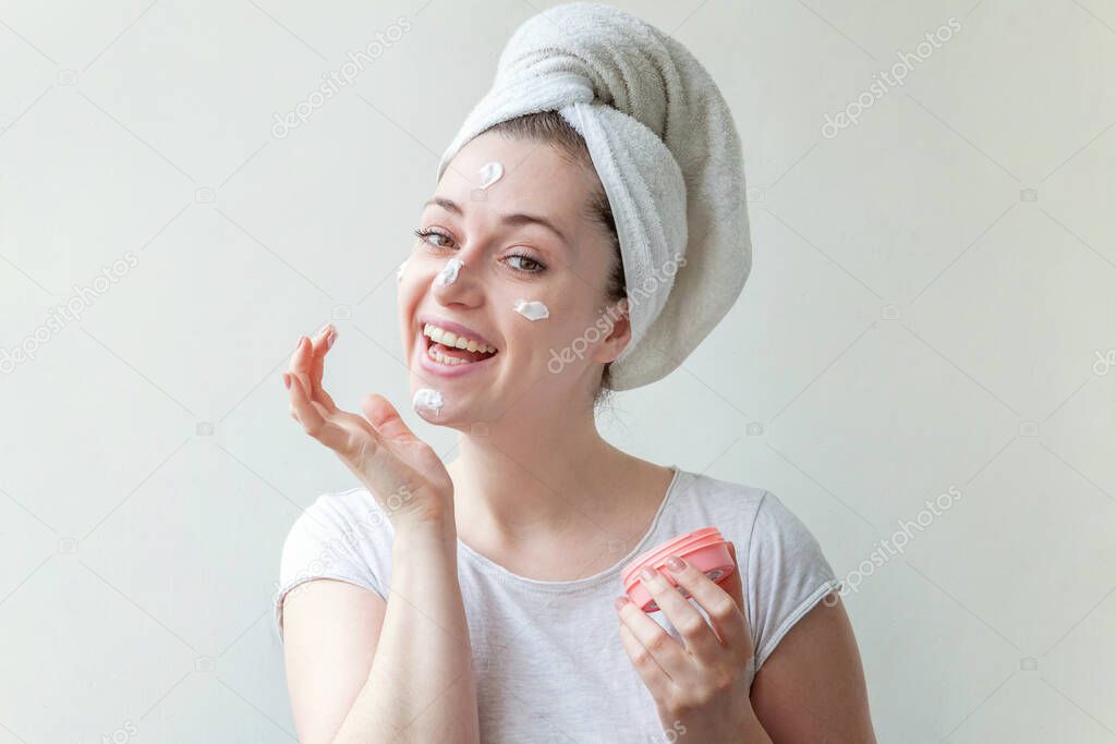 Beauty portrait of young woman in towel on head applying white nourishing mask or creme on face isolated on white background. Skincare cleansing eco organic cosmetic spa relax concept