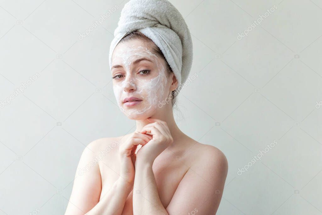 Beauty portrait of young woman in towel on head applying white nourishing mask or creme on face isolated on white background. Skincare cleansing eco organic cosmetic spa relax concept
