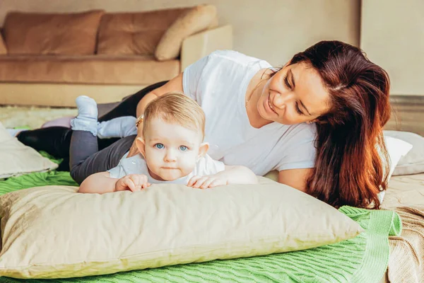 Stay Home Stay Safe. Young mother holding her child. Woman and infant little girl relaxing in white light bedroom indoors. Happy family at home. Young mom playing whith her daughter. — Stock Photo, Image