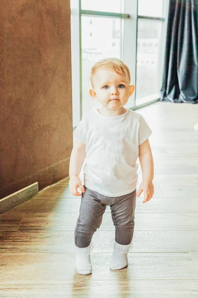 Quédese en casa. Pequeña niña bebé dulce lindo que se queda cerca de la ventana grande en la sala de estar de luz brillante en el hogar en interiores. Niñez familia maternidad ternura concepto . —  Fotos de Stock