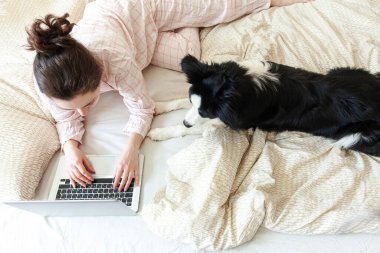 Mobil Ofis evde. Evcil köpekle pijamalı genç bir kadın evdeki bilgisayarda çalışıyor. Yaşam tarzı kızı içeride ders çalışıyor. Serbest ticaret karantina kavramı