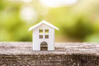 Minyatür beyaz oyuncak model ev, arka planda, yeşil arkaplanın yanında. Eco Village, soyut çevre geçmişi. Gayrimenkul ipoteği sigortası rüya ev ekolojisi kavramı