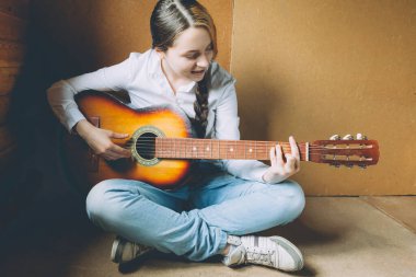 Evde kal. Kendine dikkat et. Genç bir kadın yerde oturuyor ve evde gitar çalıyor. Genç kız şarkı çalmayı ve şarkı yazmayı öğreniyor. Hobi yaşam tarzı rahatla Enstrüman eğlence eğitimi konsepti