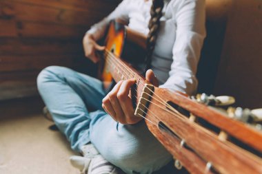 Evde kal. Kendine dikkat et. Genç bir kadın evde oturup gitar çalıyor, elleri yakın. Genç kız şarkı çalmayı ve şarkı yazmayı öğreniyor. Hobi yaşam tarzı rahatla Enstrüman eğlence eğitimi konsepti
