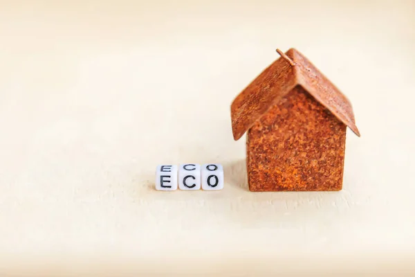 Miniature toy model house with inscription ECO letters word on wooden backdrop. Eco Village abstract environmental background. Ecology zero waste social responsibility recycle bio home concept
