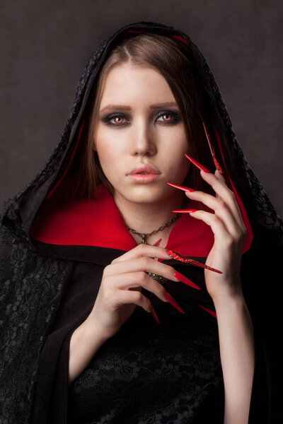 Vintage style portrait of young beautiful vampire woman with gothic Halloween makeup. Manicured red stilettos nails.
