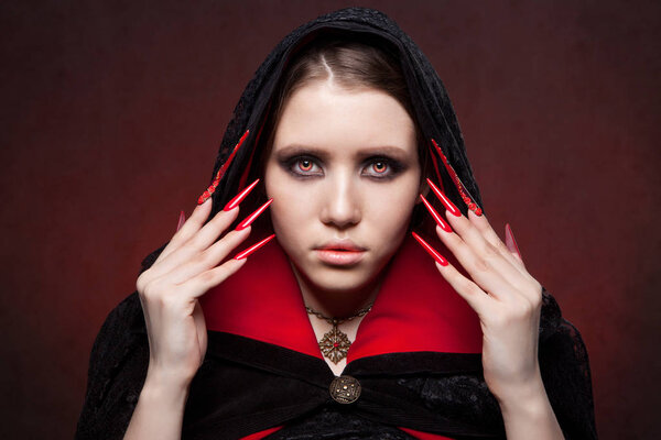 Vintage style portrait of young beautiful vampire woman with gothic Halloween makeup. Manicured red stilettos nails.