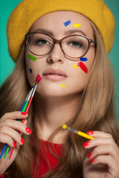 Portrait of a woman with colorful paint brushstroken on face. Bright green eyes. — Stockfoto