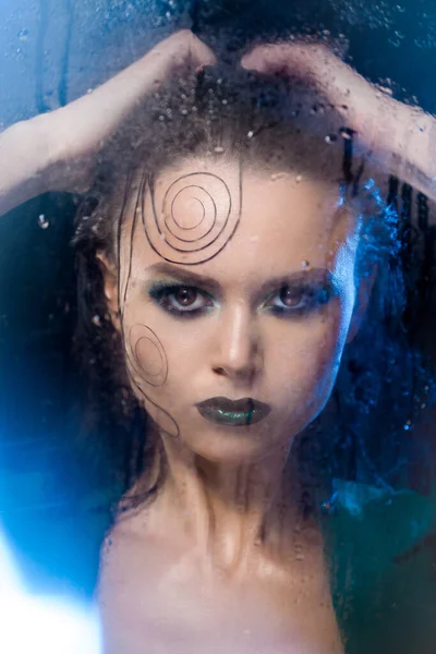 Beautiful model girl stands behind a glass with raindrops. — Stock Photo, Image