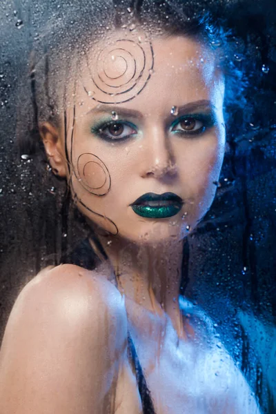Vacker modell flicka står bakom ett glas med regndroppar. — Stockfoto