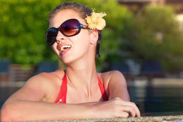 Beautiful young woman in sunglasses with flower in hair smiling in luxury pool — Stock Photo, Image