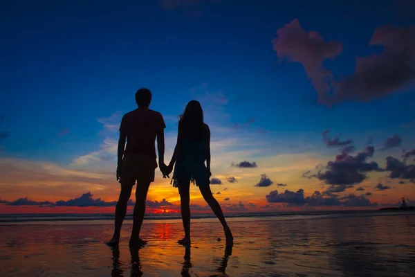 Sunset silhouette of young couple in love holding hands at beach — Stock Photo, Image