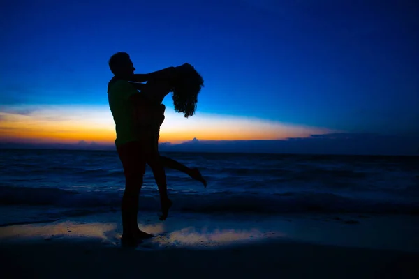 Sunset silhouette of young couple in love hugging at beach — Stock Photo, Image