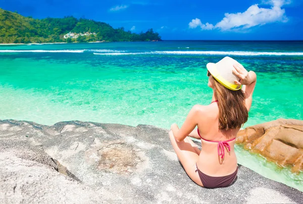 Joven mujer de pelo largo en traje de baño de una sola pieza relajándose en las rocas sobre el mar. Isla Mahe, Seychelles —  Fotos de Stock