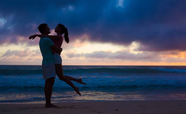 Sunset silhouette of young couple in love hugging at beach — Stock Photo, Image