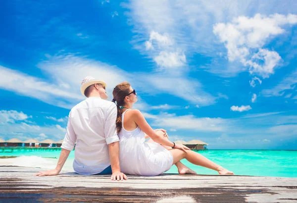 Vista traseira do casal sentado na ponte de madeira pela praia tropical em Maldivas — Fotografia de Stock