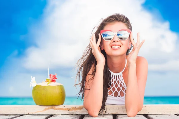 Long haired woman in bikini and sunglasses with fresh coconut cocktail relaxing on tropical beach — Stock Photo, Image