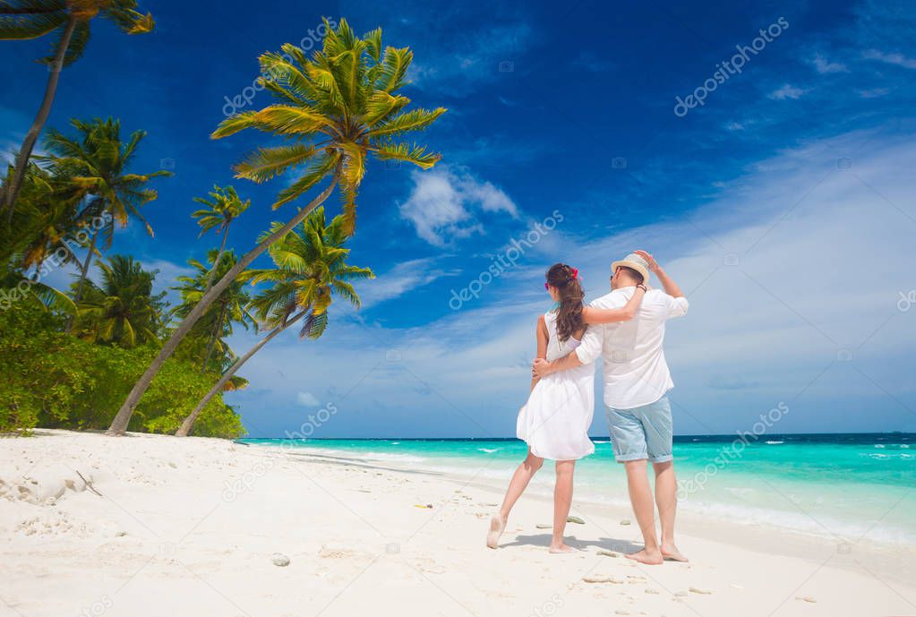 happy young couple in white clothes walking by the beach. Maldives