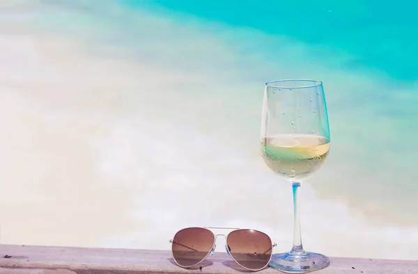 Glas gekoelde witte wijn en zonnebril op tafel op een tropische achtergrond — Stockfoto