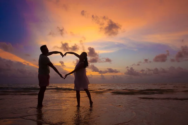 在海滩拥抱的年轻夫妇的日落轮廓 免版税图库照片