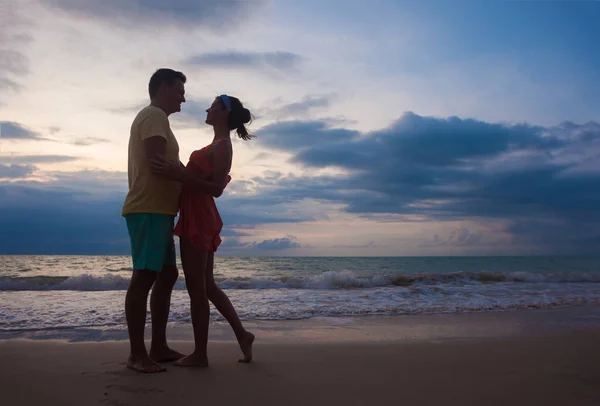 Solnedgång silhuett av unga par i kärlek kramas på stranden — Stockfoto