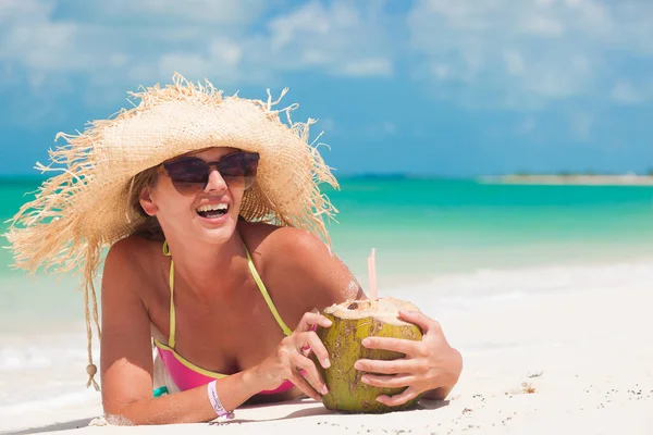 Glad ung kvinna ler i halmhatt med kokoscocktail på stranden — Stockfoto