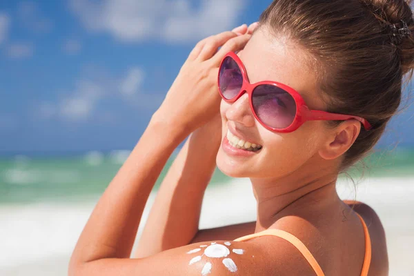 Närbild på ung kvinna i solglasögon att sätta solen grädde på axeln — Stockfoto