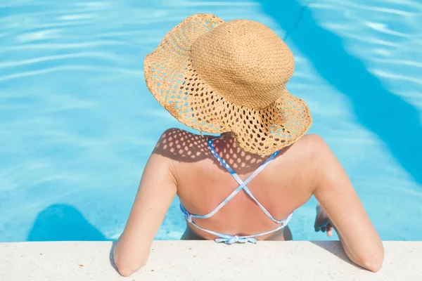 Menina de chapéu de palha sentado na piscina — Fotografia de Stock