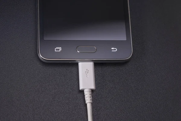 Smartphone negro sobre fondo negro con cable blanco —  Fotos de Stock