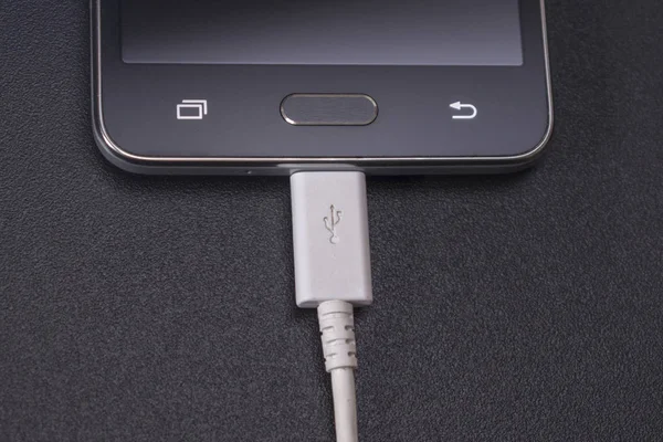 Smartphone negro sobre fondo negro con cable blanco —  Fotos de Stock