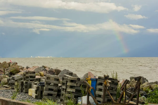 garbage on the shore of the pond of the sea on the horizon city and rainbow