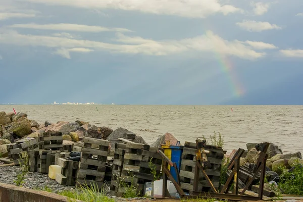 garbage on the shore of the pond of the sea on the horizon city and rainbow