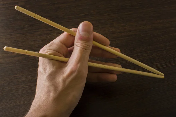 La mano izquierda de un hombre usando palillos de bambú sobre un fondo de madera —  Fotos de Stock