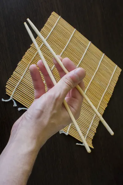 Palillos en la mano en el fondo de una estera de sushi de bambú — Foto de Stock