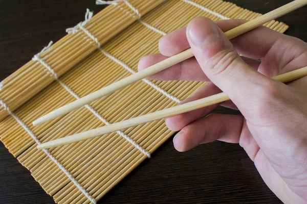Chopsticks in hand in the background of a bamboo sushi mat — Stock Photo, Image