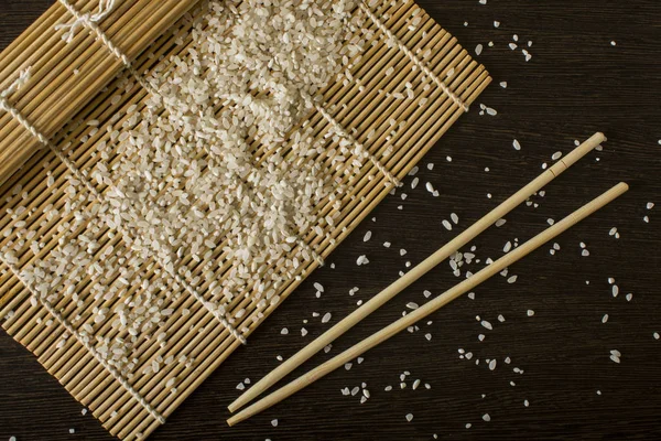 A sushi mat on which scattered rice next to lies chopsticks — Stock Photo, Image