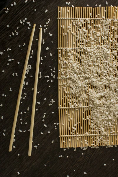 Коврик для суши, на котором разбросан рис рядом с палочками для еды — стоковое фото