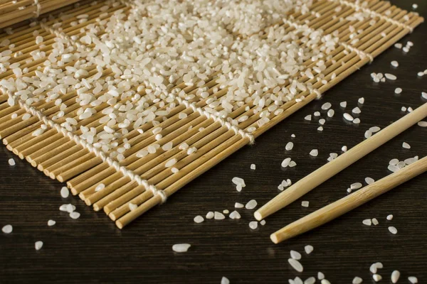 A sushi mat on which scattered rice next to lies chopsticks — Stock Photo, Image