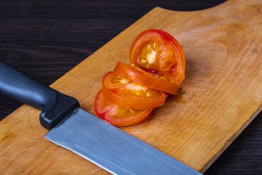 karanlık bir tablo üzerinde bir bıçak ve bir kesme tahtası ile kısmen kesilmiş domates