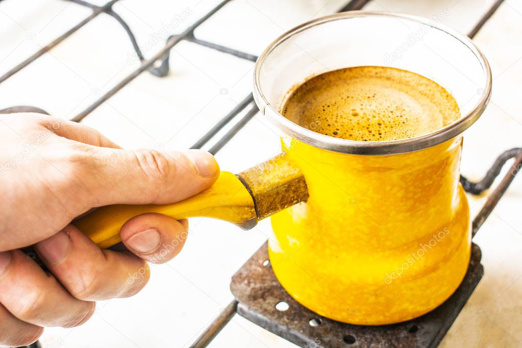 in his hand a yellow Turk with coffee on the stove.