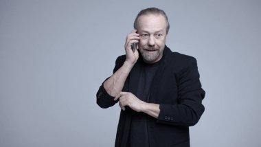 Neşeli, sakallı, beyaz adam telefonda konuşuyor.