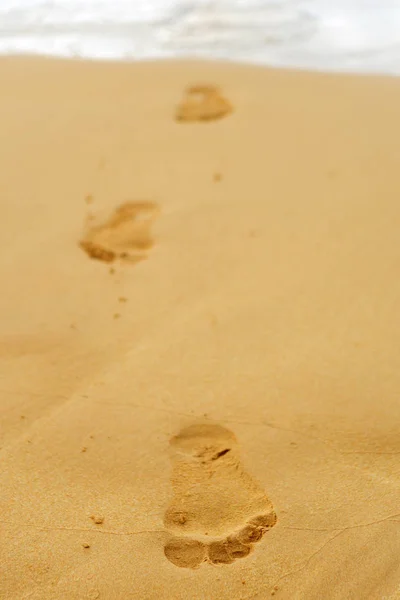 Huellas de los pies desnudos de un hombre en la arena del océano al th —  Fotos de Stock