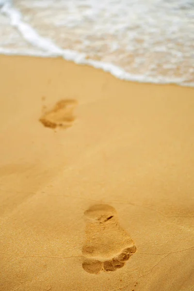 Huellas de los pies desnudos de un hombre en la arena del océano al th —  Fotos de Stock