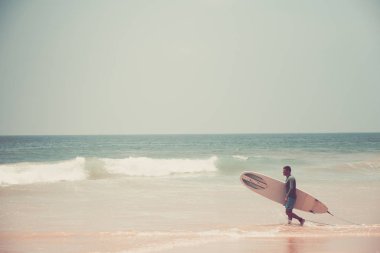 Hikkaduwa. Sri Lanka. 06 Mart 2018. Plajda sörf tahtası ile bir sörfçü yürür.